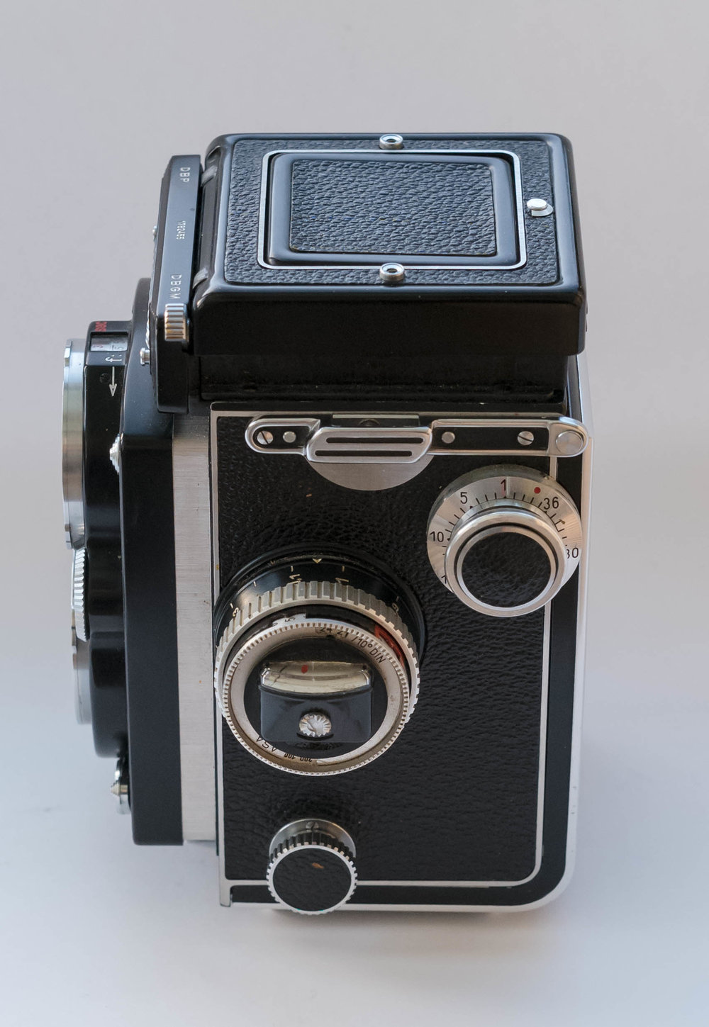 Side of the camera with the exposure meter. It has different ranges for normal light values and low light values. These are set by the switch on the top left of the camera body, called a sensitivity range control. For low values the EV is read from a red window after a red and black needle have been matched. For normal light values the value is read from a black window. This may seem complicated, but it becomes second nature very quickly. On the top right side of the camera is a counter for 35mm film. I won’t go into the use of the Rolleikin 35mm adapter kit or the changing of the pressure plate for 35mm as, in truth, I cannot see why anyone would use 35mm film on a Rolleiflex, except, perhaps, if they had run out of 120 film